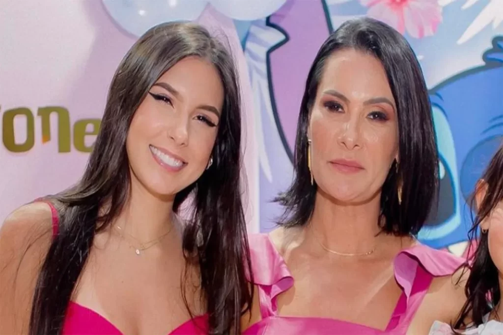 Ana Castela sorrindo com cabelo liso, ao lado de sua mãe Michele Castela em vestido rosa vibrante, em festa infantil.