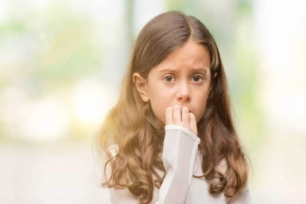 Menina com expressão de preocupação e ansiedade roendo as unhas ou mordendo o dedo.
