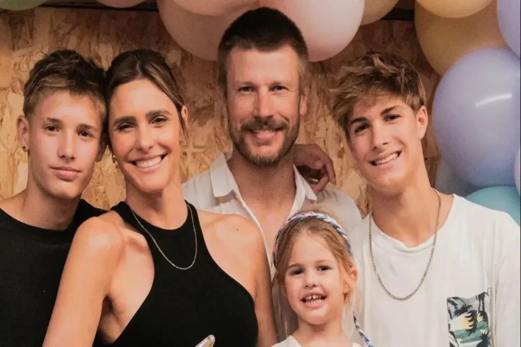 A apresentadora brasileira Fernanda Lima e seu marido Rodrigo Hilbert posam sorridentes com seus três filhos (dois adolescentes e uma menina pequena) em uma foto de família em frente a balões de festa.