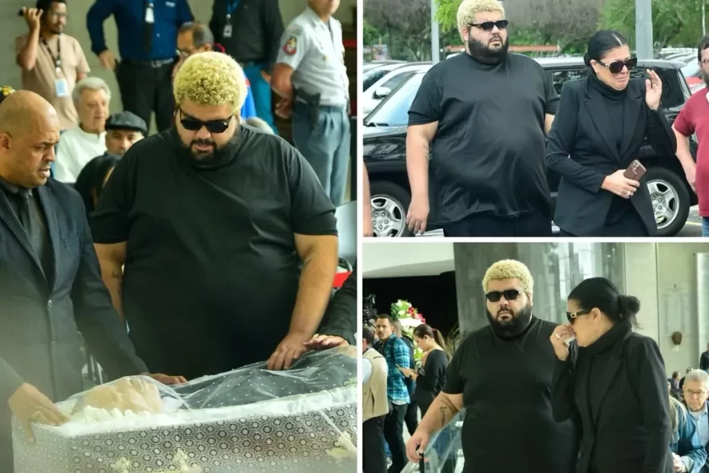 Um collage de três fotos mostrando os filhos do ex-boxeador Maguila em um funeral. Em primeiro plano na imagem principal, um homem de barba e cabelo descolorido, vestindo uma camiseta preta e óculos de sol, está curvado sobre um caixão. Em duas fotos menores, ele aparece ao lado de uma mulher de cabelo escuro, também de preto e óculos de sol. Ambos demonstram tristeza e luto durante a cerimônia de despedida.