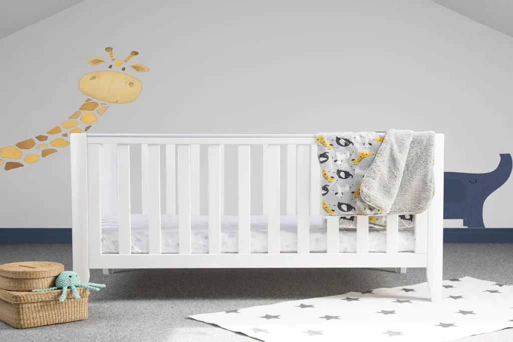 Quarto de bebê iluminado com um berço de madeira clara e branca, uma poltrona de amamentação cinza ao lado e três quadros de animais fofos decorando a parede branca ao fundo.