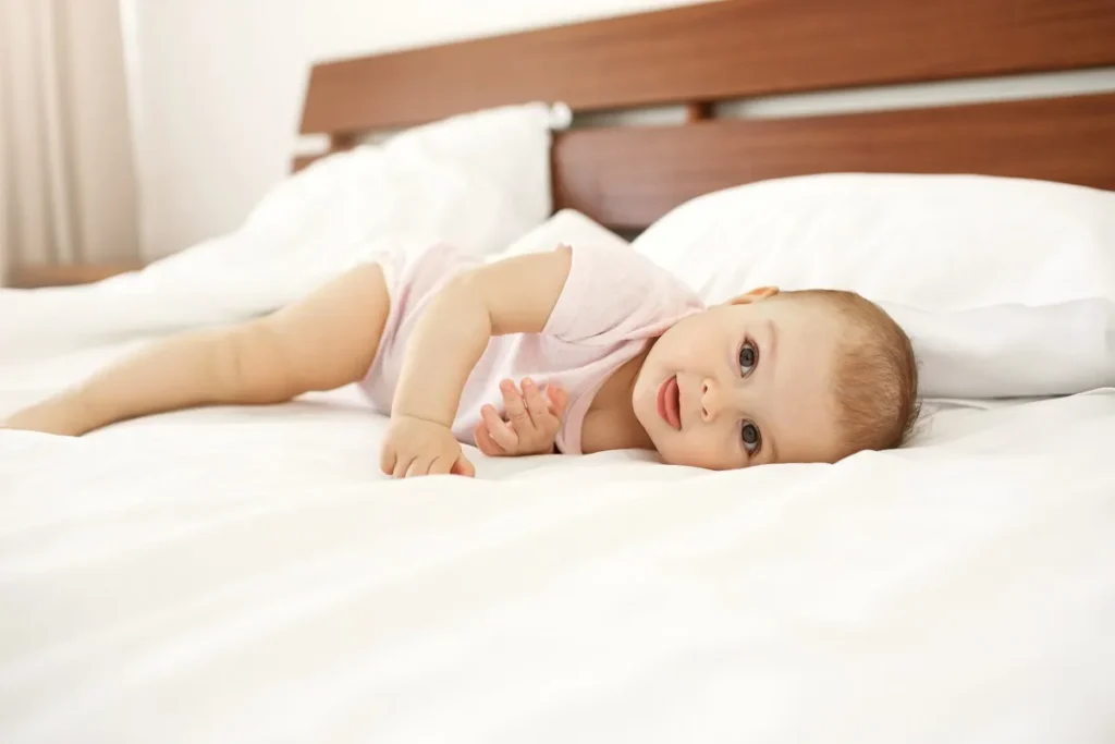 Duas mãos masculinas ajustando e pressionando o canto de um colchão cinza e branco sobre o estrado de ripas de madeira clara de uma cama ou berço.