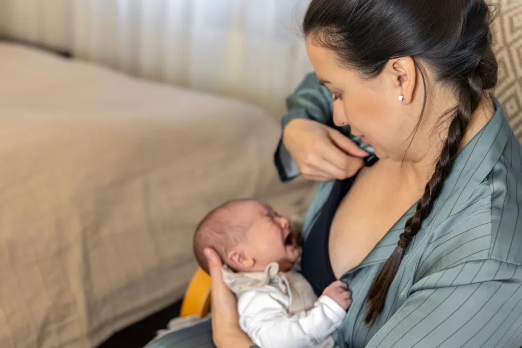 Visão em ângulo superior de mãe ajustando a roupa para amamentar o bebê chorando no colo.