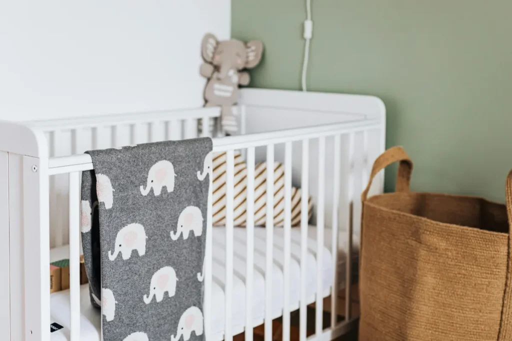 Berço infantil branco com manta estampada e colchão montado em quarto decorado para bebê.