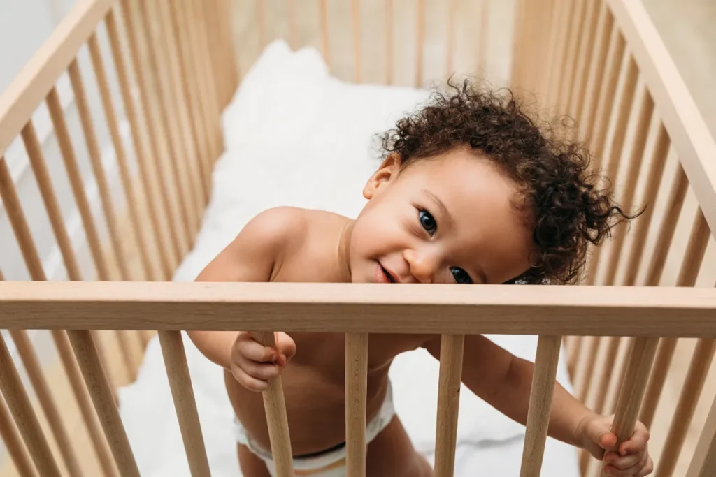 Criança maior em pé dentro do berço demonstrando fase próxima da transição para cama infantil segura