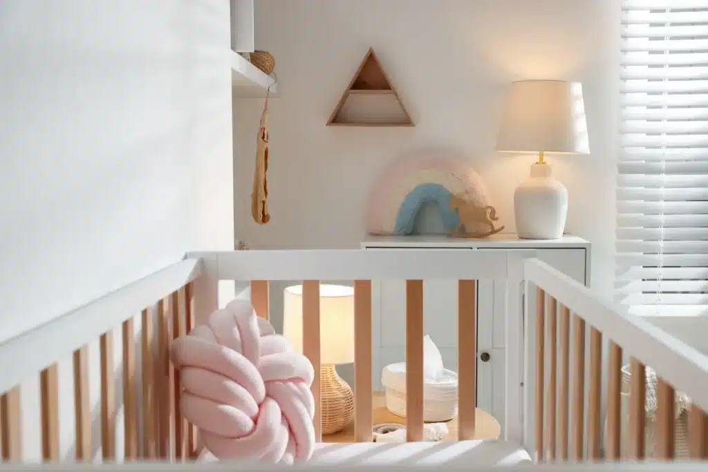 Berço de madeira clara em quarto de bebê minimalista com luminária, nichos decorativos e tons pastel.