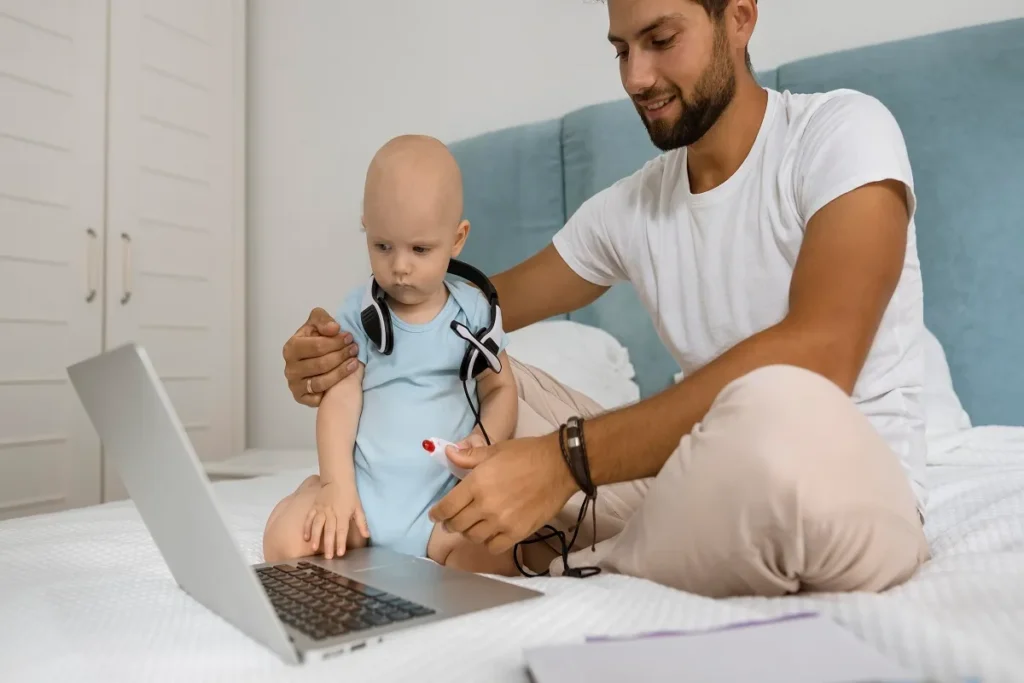 Pai e bebê sentados na cama olhando para um laptop aberto, ilustrando a importância de verificar a segurança digital e criptografia em dispositivos de monitoramento infantil.