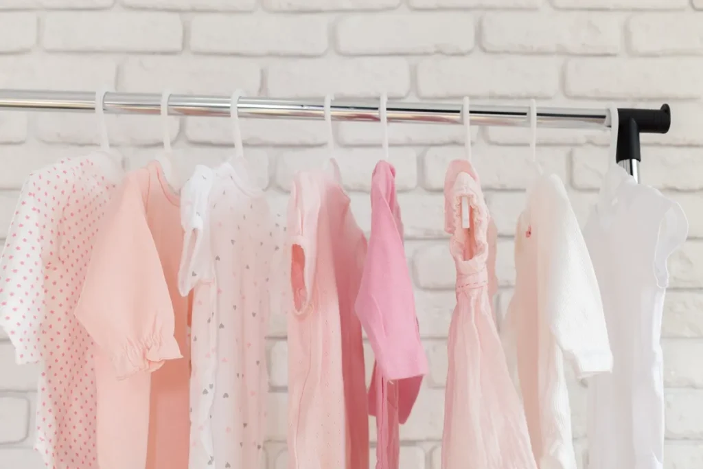 Guarda-roupa planejado de bebê com as portas abertas, revelando roupas penduradas em cabides, nichos organizadores com caixas cinzas e iluminação interna embutida.