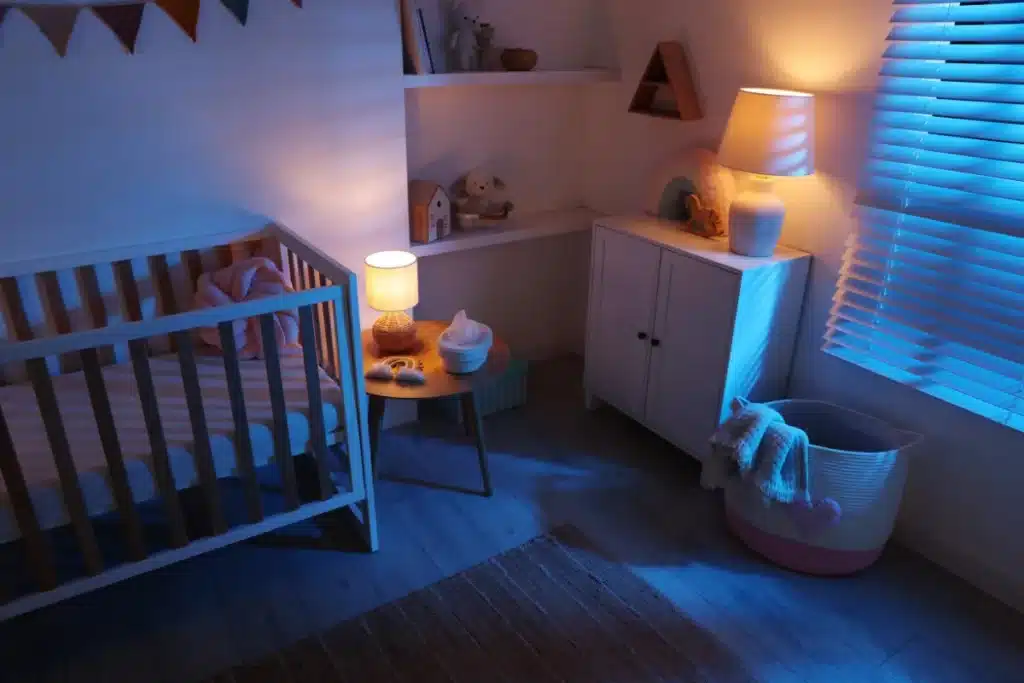Quarto de bebê iluminado à noite com luz suave, berço branco e decoração aconchegante.