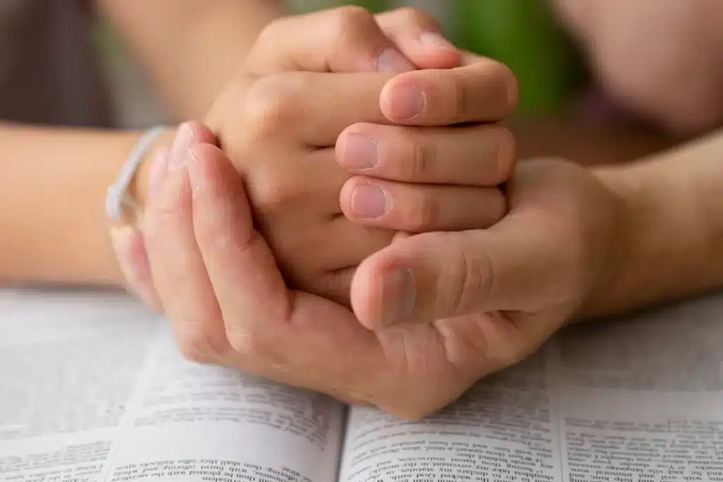 Mãos entrelaçadas em oração sobre uma Bíblia aberta simbolizando fé, espiritualidade e união familiar