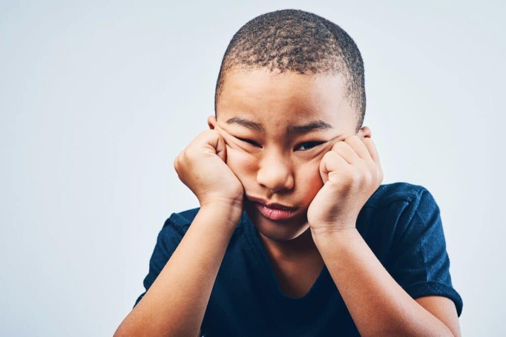Menino com expressão de tédio apoiando o rosto nas mãos, representando criança de 7 anos sem estímulo ou procurando algo para brincar.