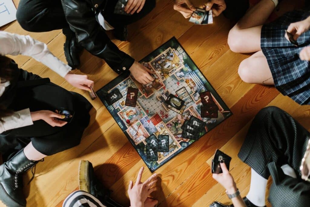 Crianças reunidas no chão jogando jogo de tabuleiro com cartas e peças, opção de brinquedo para criança de 7 anos.