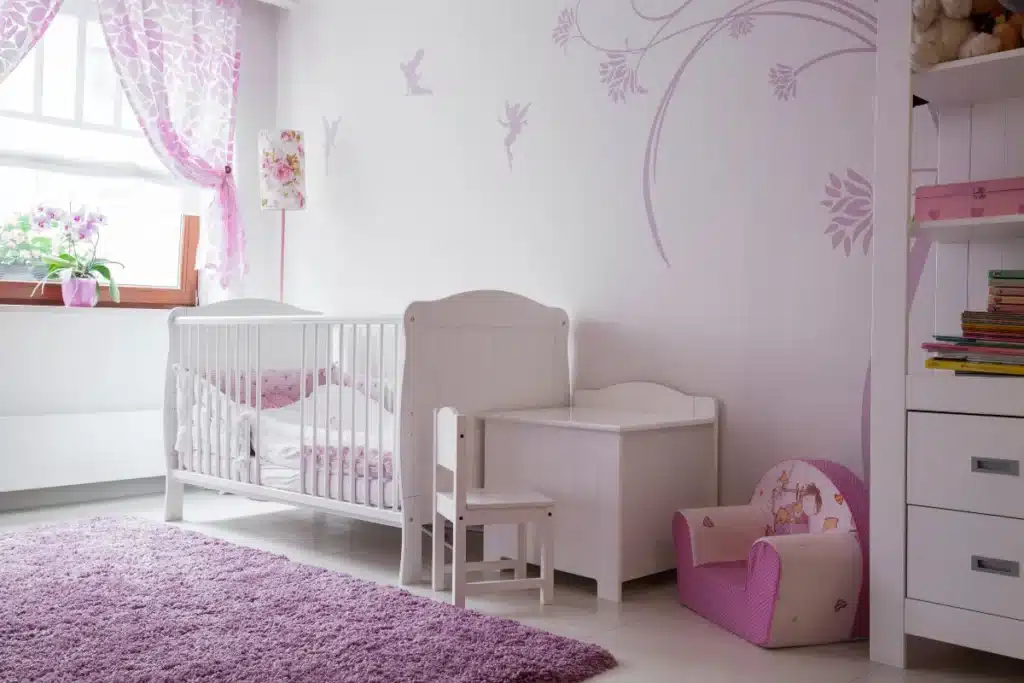 Quarto de bebê feminino com decoração rosa clara, berço branco e móveis infantis delicados.