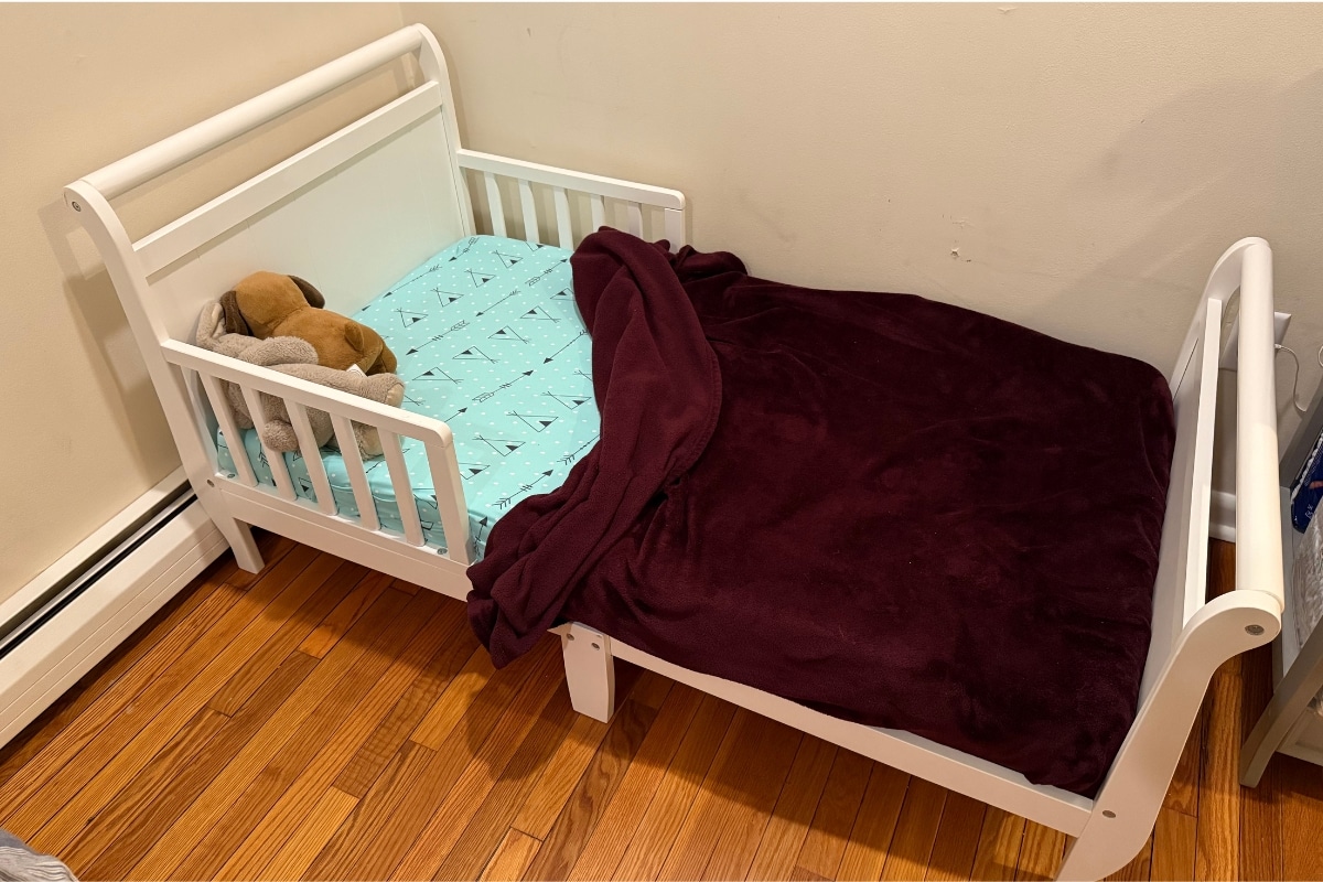 Cama infantil branca com grades laterais baixas em um quarto residencial.