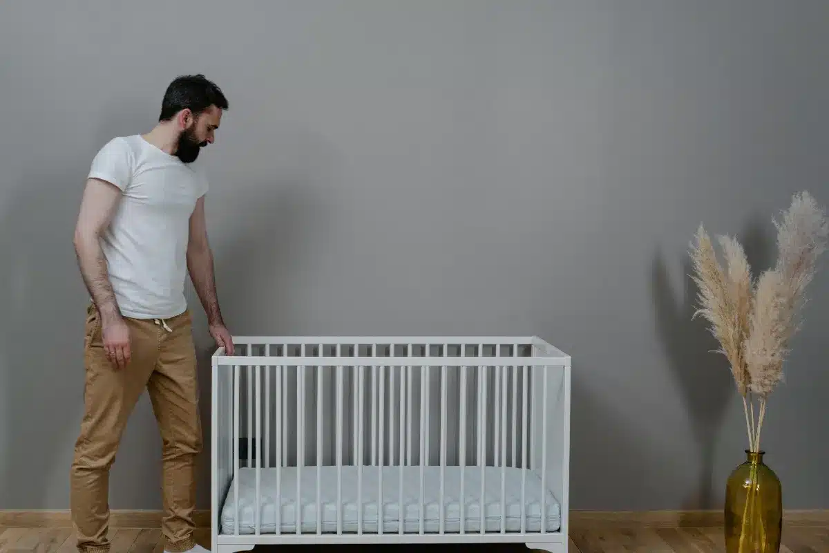 Adulto ao lado de um berço branco preparado para a rotina de sono do bebê