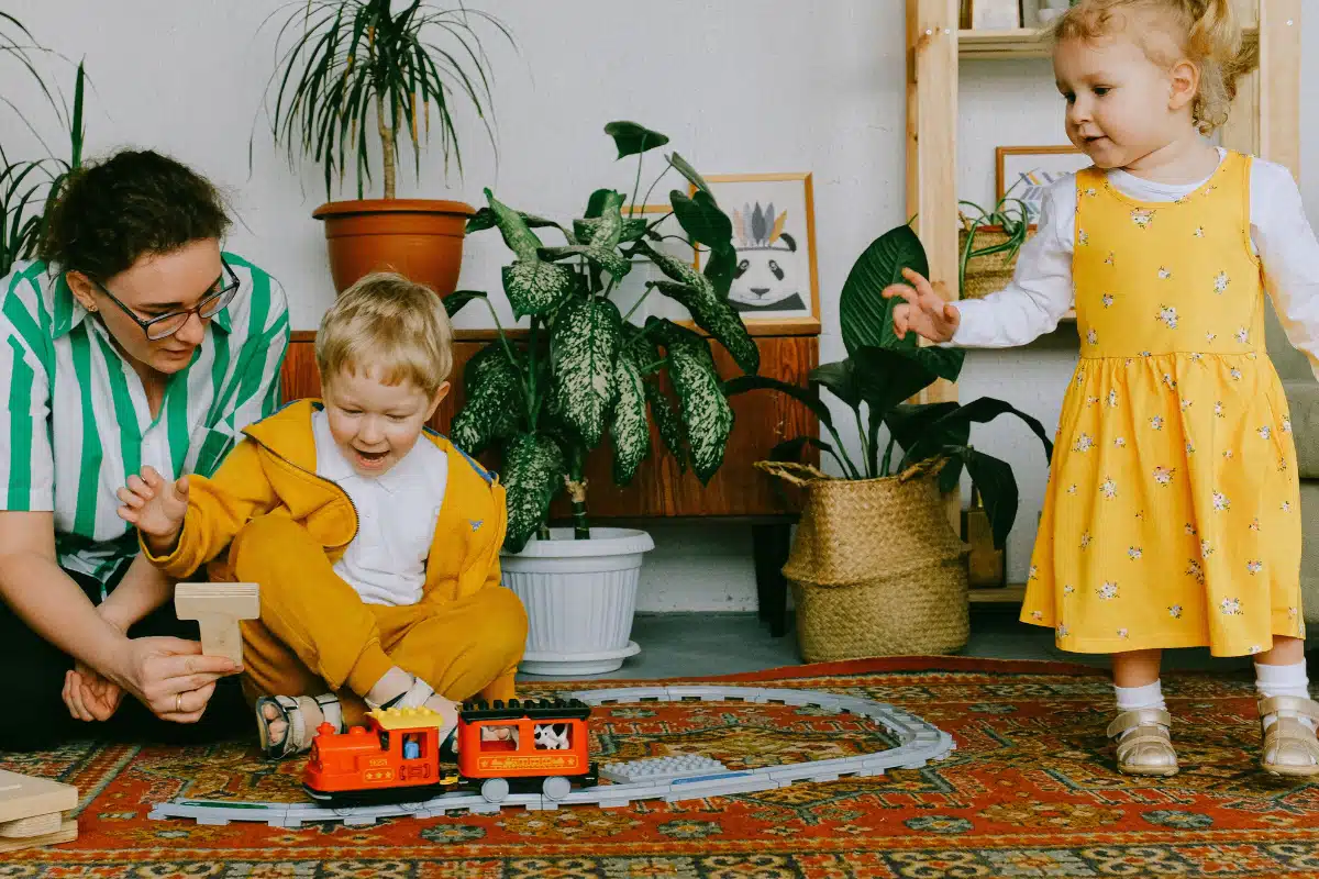 Mãe sentada com duas crianças enquanto elas brincam juntas com um trem de brinquedo