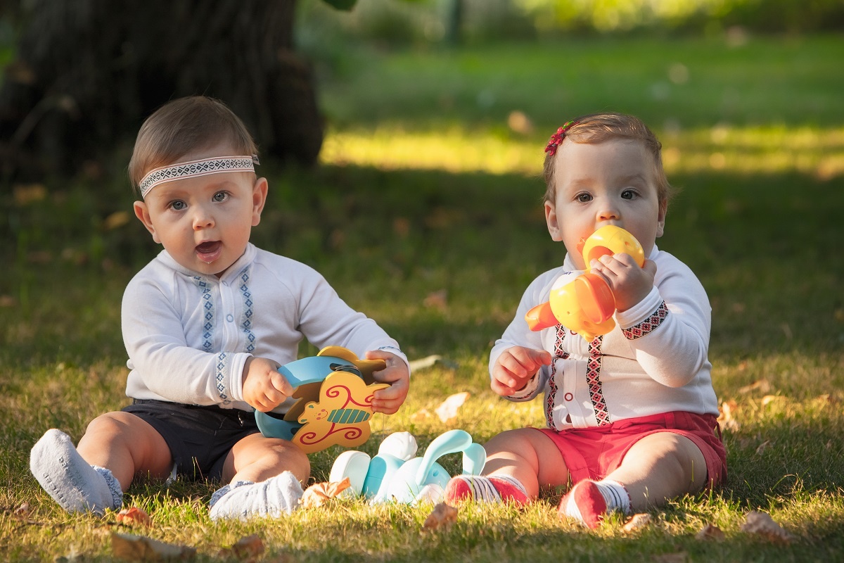 dois bebês, um menino e uma menina sentados rodeados de brinquedos