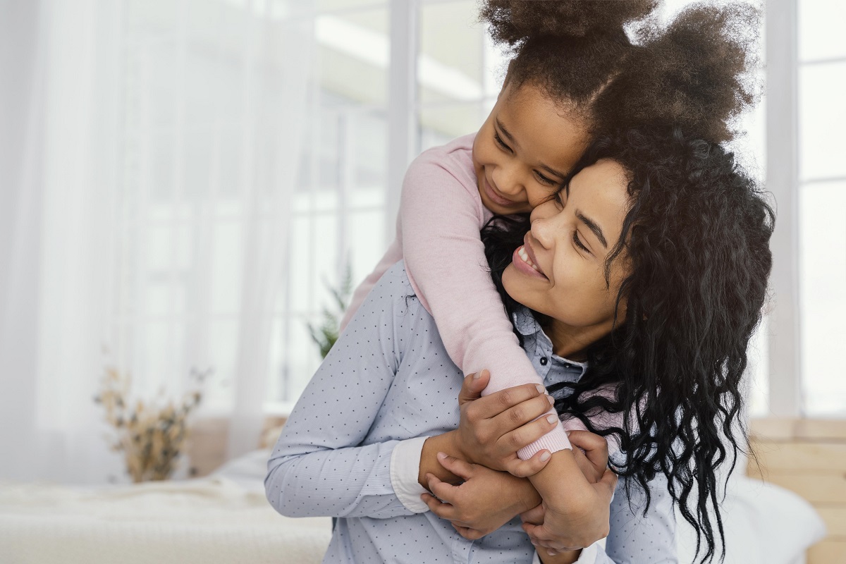 vista frontal de uma mulher sendo abraçada por uma menina, as duas estão sorrindo