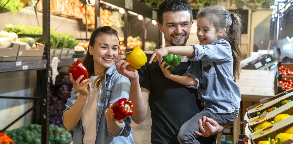 uma mulher e um homem sorrindo ele está com uma criança no colo, todos estão segurando verduras