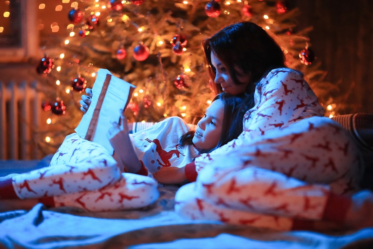 uma mulher e uma menina deitadas lendo um livro e usando pijamas iguais