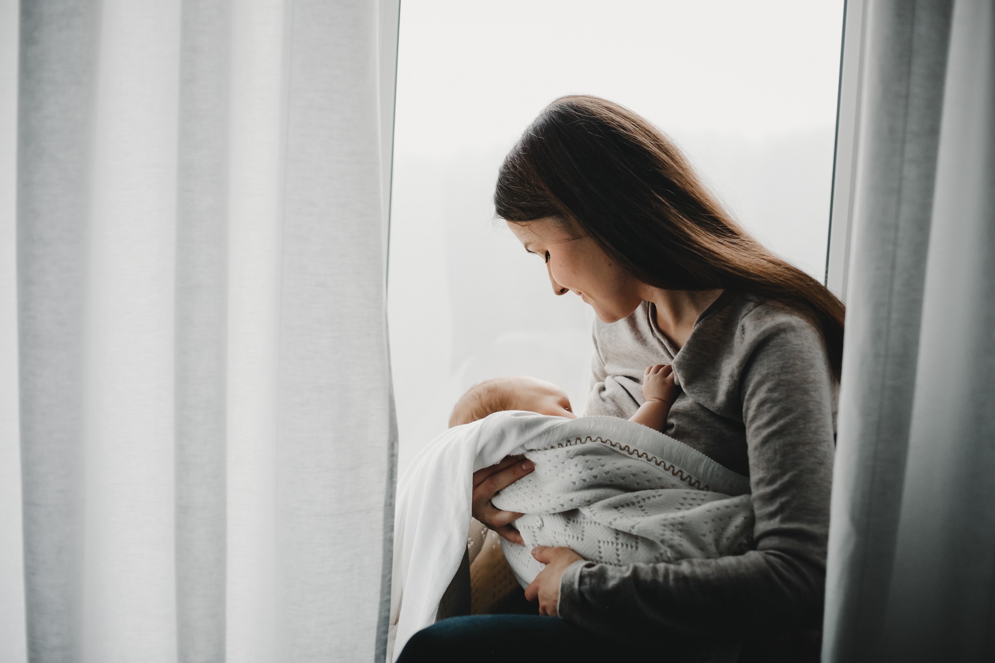 mulher sentada com a cabeça inclinada segurando um bebê recém nascido nos braços