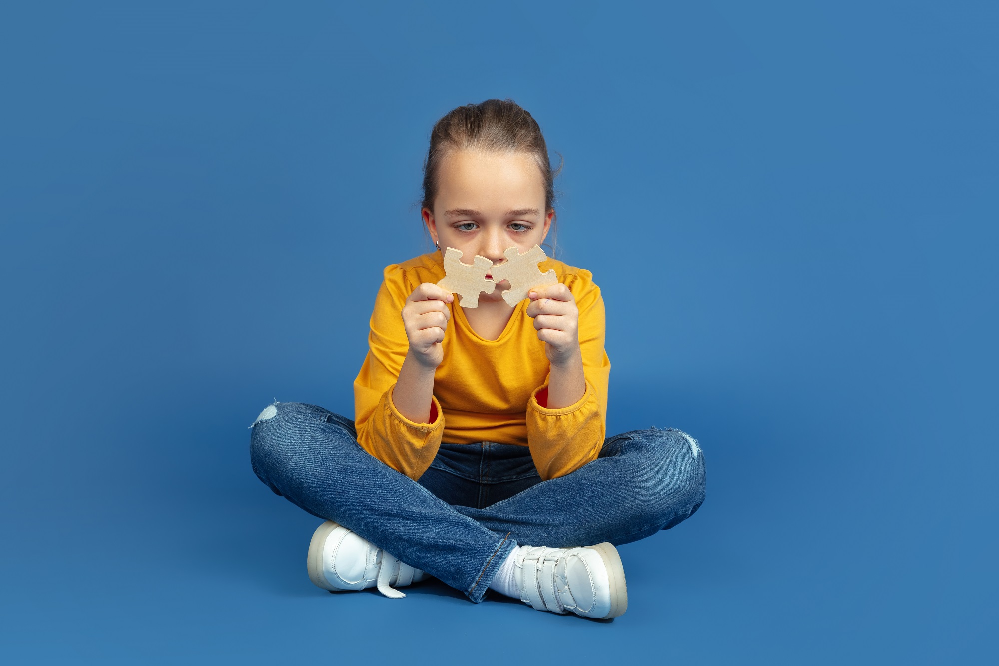 Sinais de Autismo Retrato de uma menina triste sentada isolada no fundo azul