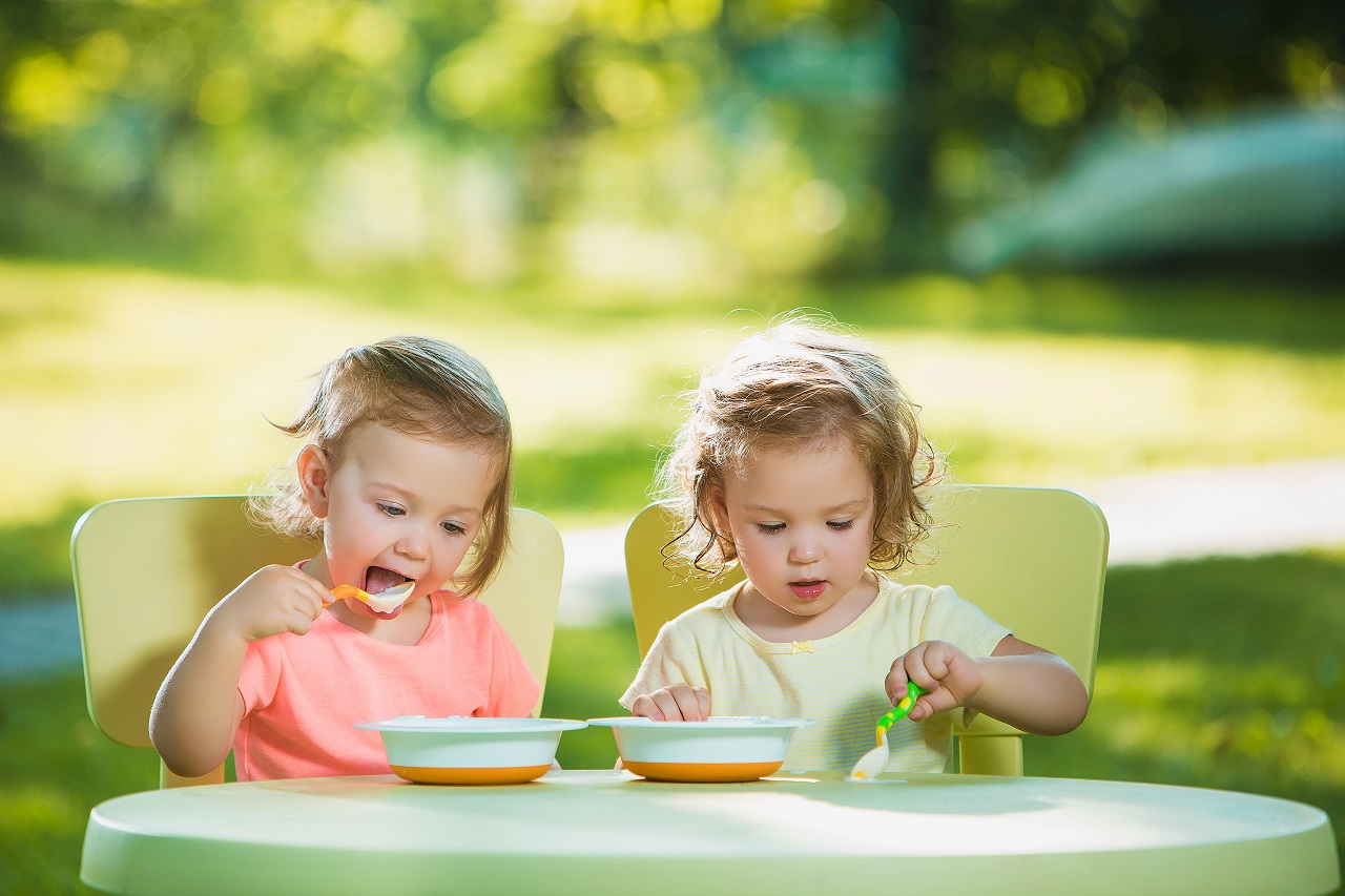 Duas meninas sentadas à mesa comendo juntas no gramado verde