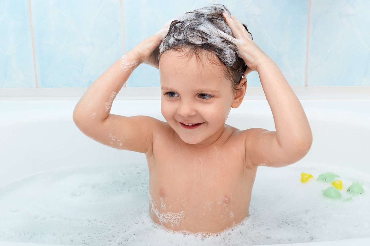 menina criança em uma banheira lavando os cabelos cheios de espuma de shampoo