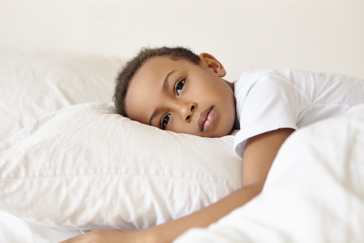 um menino deitado em uma cama abraçando um travesseiro branco com uma expressão triste