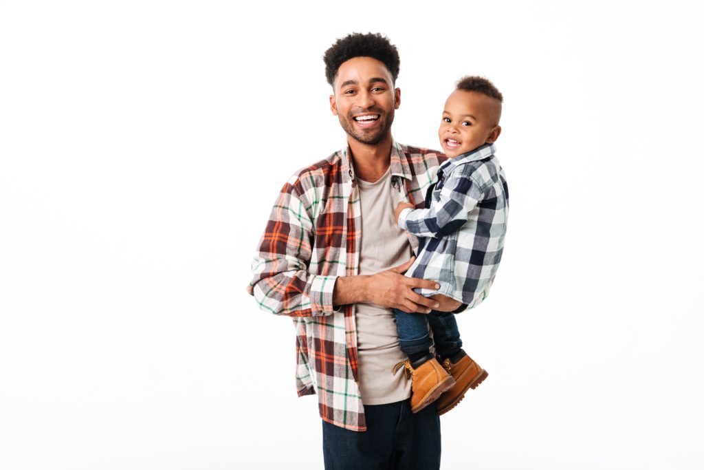 jovem africano adulto de pé com um menino africano no colo ambos sorrindo de camisa xadrez