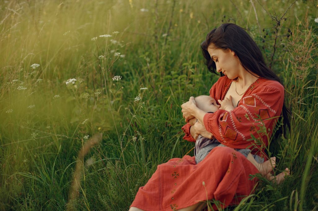 mulher morena em um campo amamentando um bebê