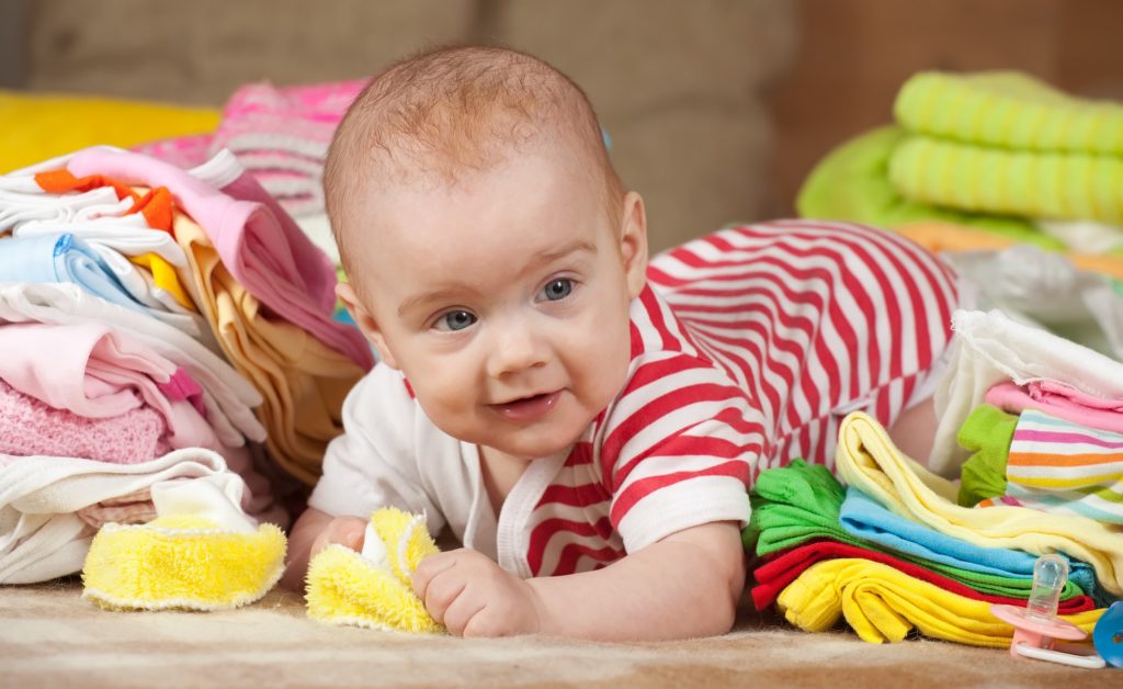 lindo bebê deitado em meio a várias roupinhas de bebê