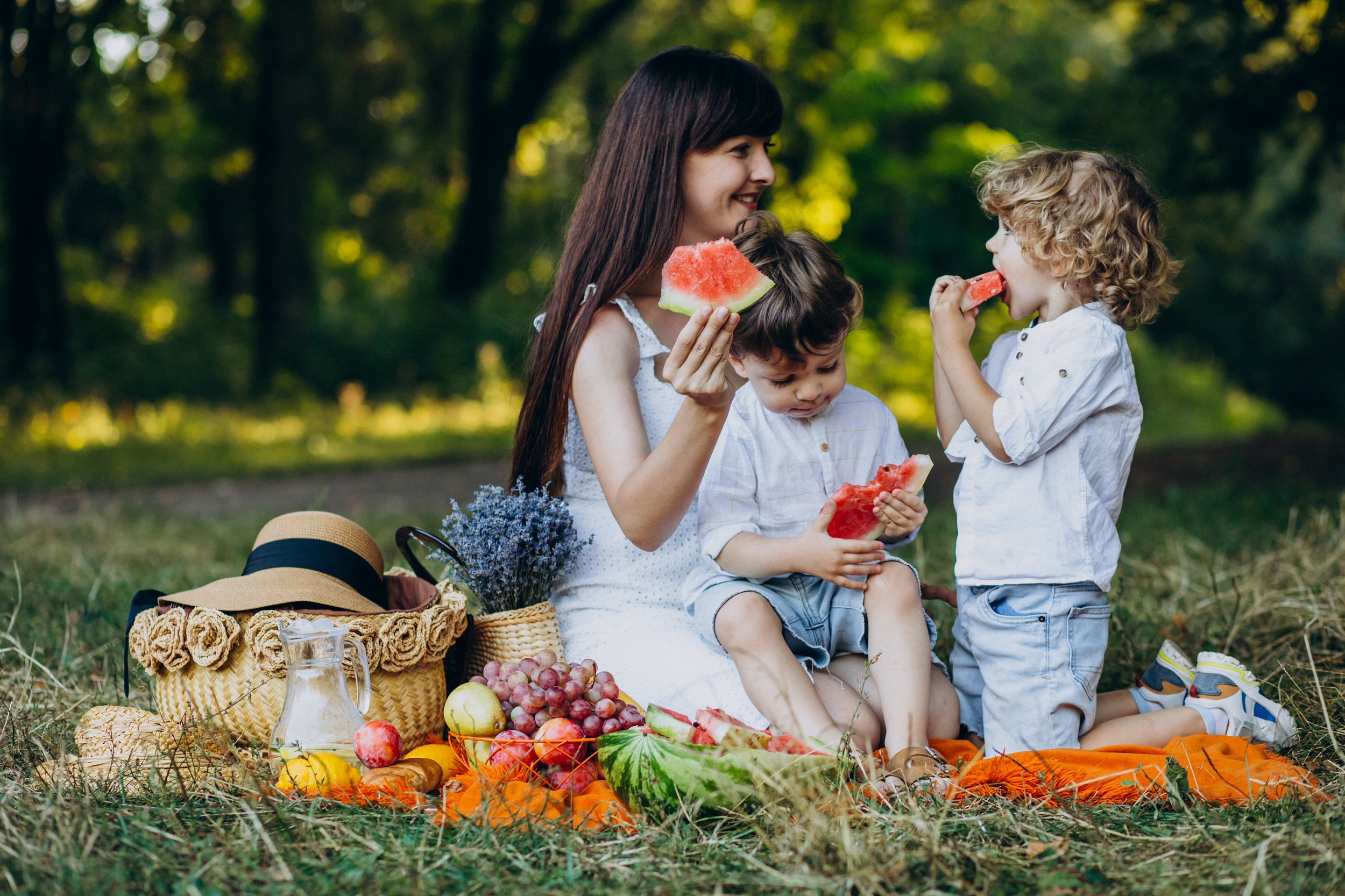 mulher fazendo um piquenique com dois meninos no parque comendo melância