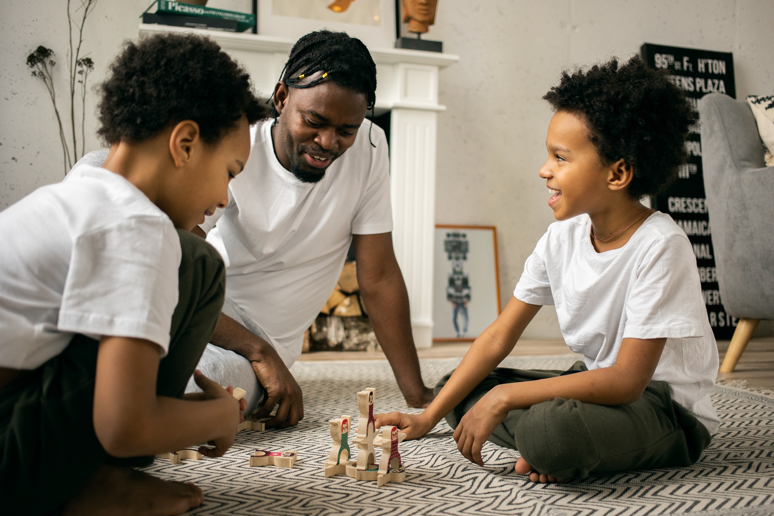 homem negro sentado no chão com dois jovens afros jogando um jogo