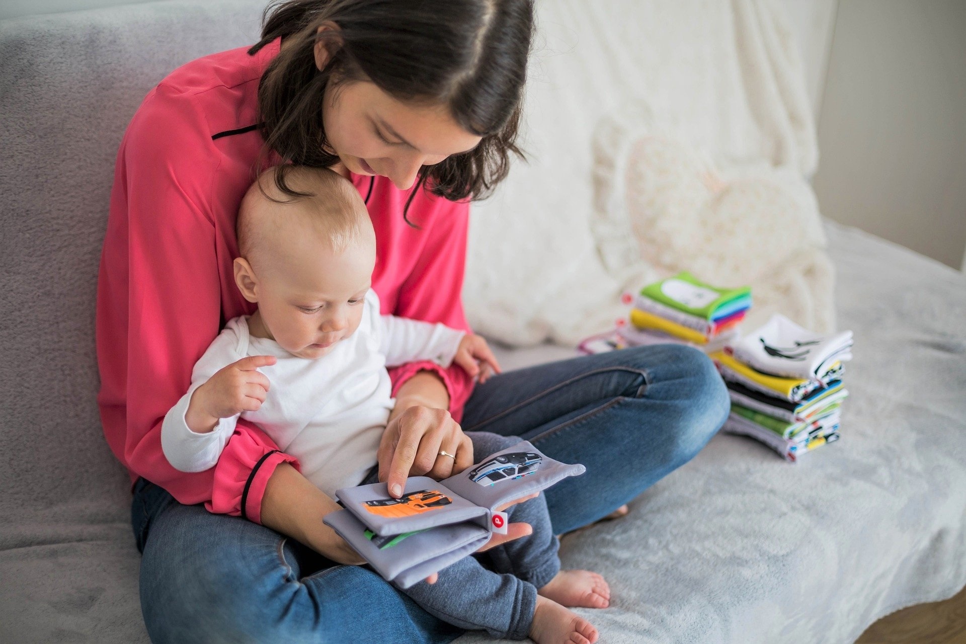 mulher no sofá com um bebê no colo mostrando a ele um livro infantil