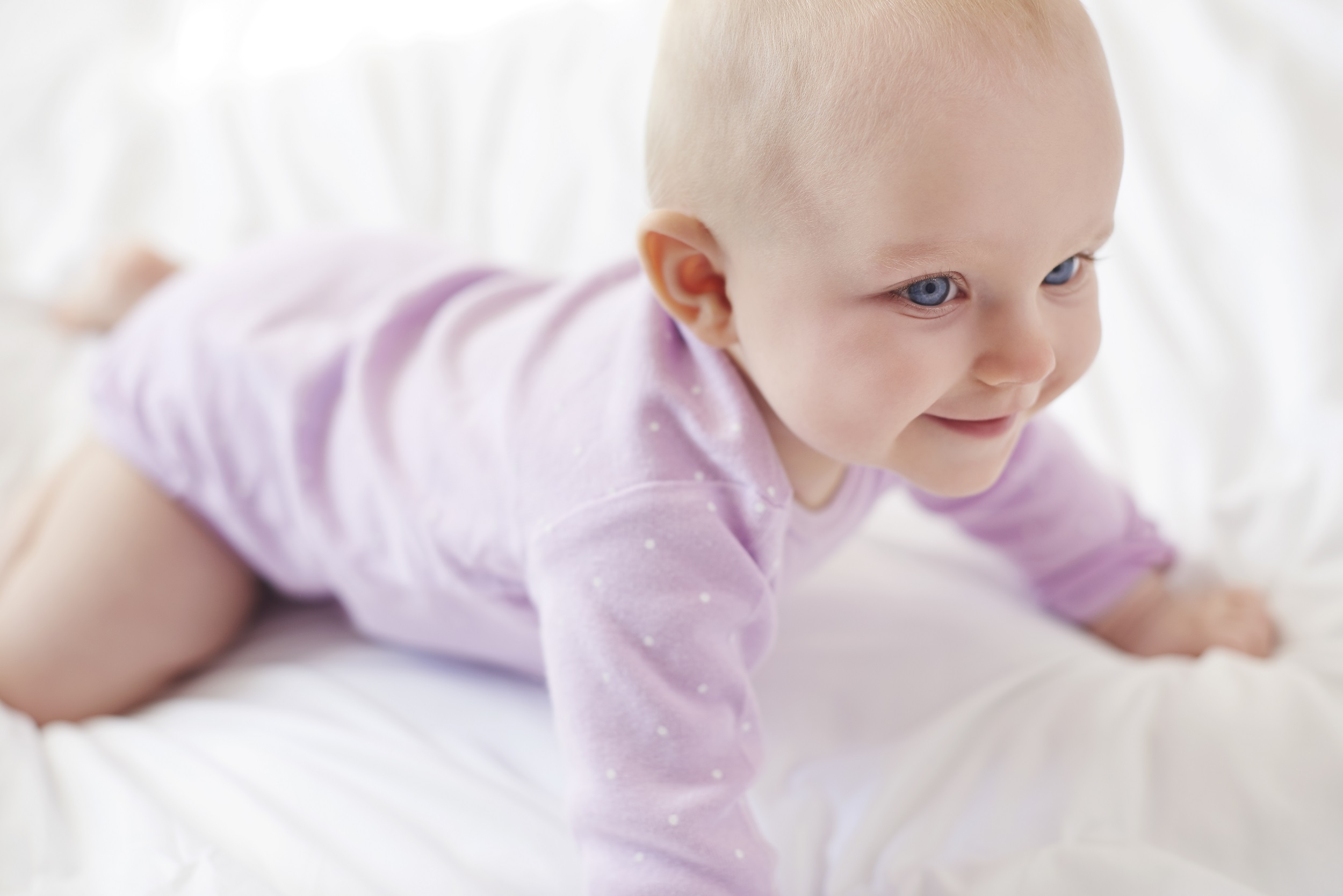 bebê menina sorrindo de olhos azuis está tentando engatinhar