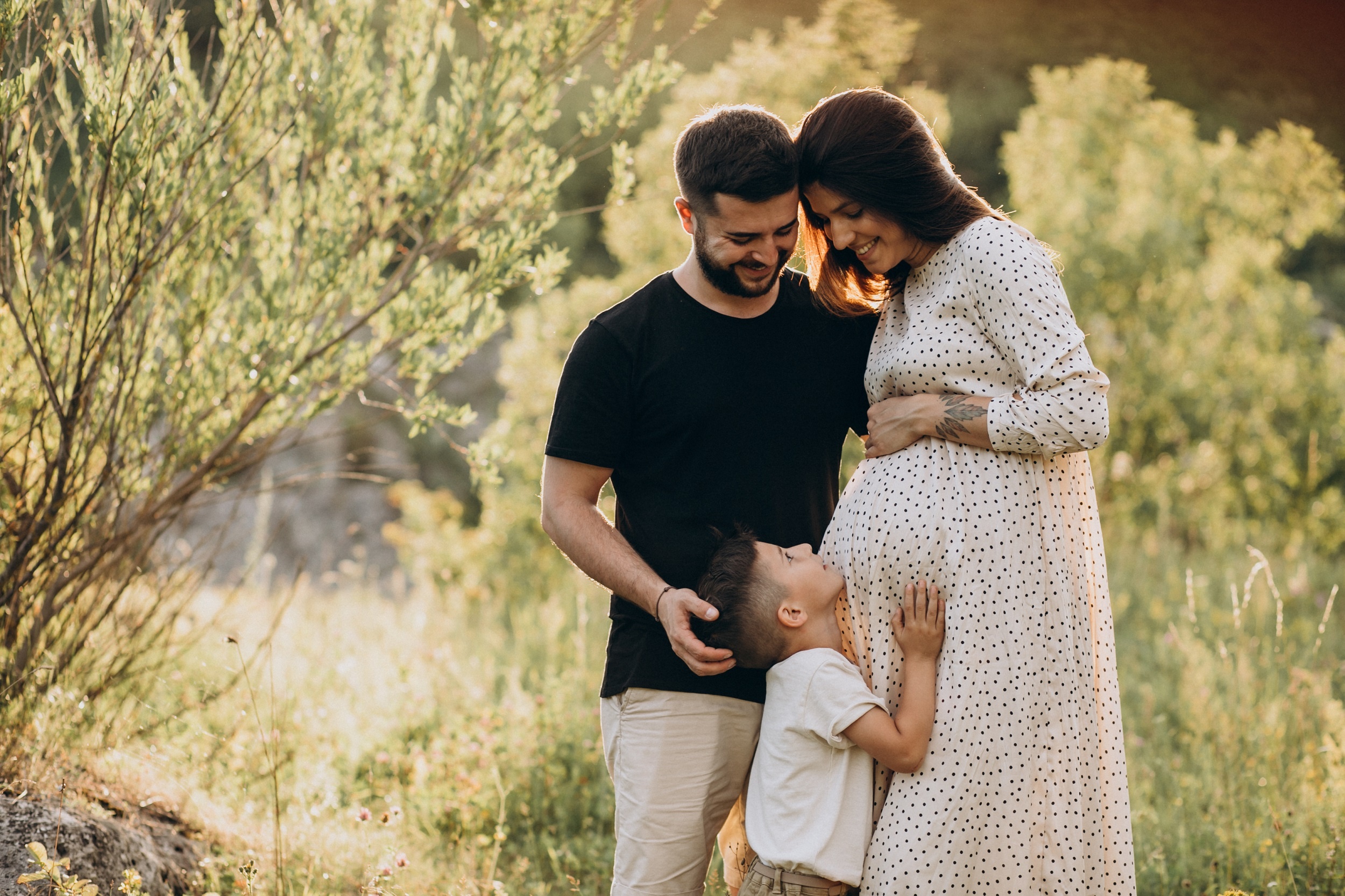 linda família reunida, um homem jovem, uma mulher morena jovem grávida e um menino pequeno com as mãos na barriga da mulher