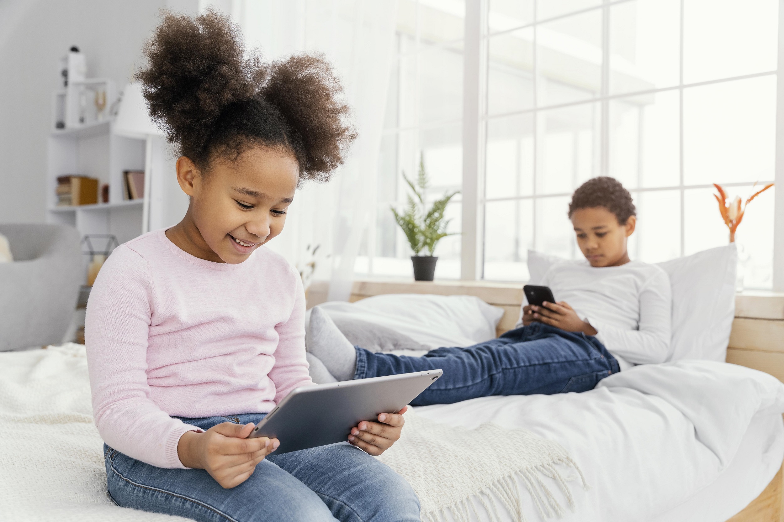 duas crianças afro o menino está com um celular e a menina com um tablet