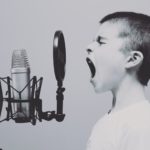 imagem em preto e branco de um menino gritando em um microfone