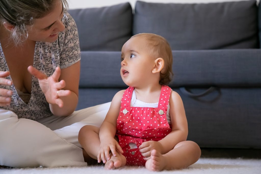 mulher sentada no chão sorrindo e falando com uma bebê que a encara