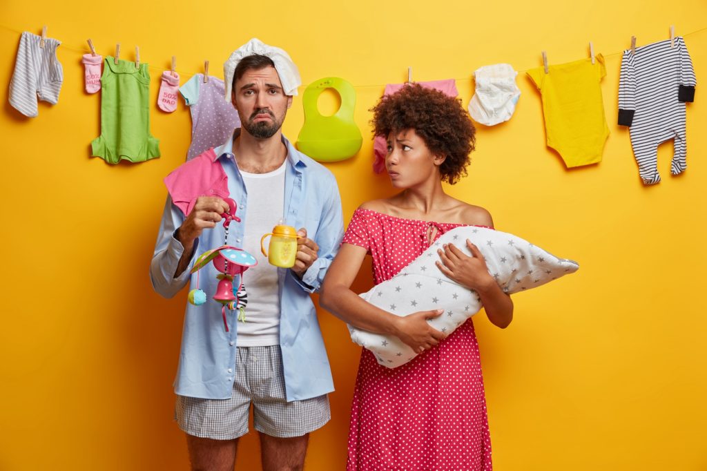 homem e mulher em um fundo amarelo com um varal cheio de roupinhas de bebê