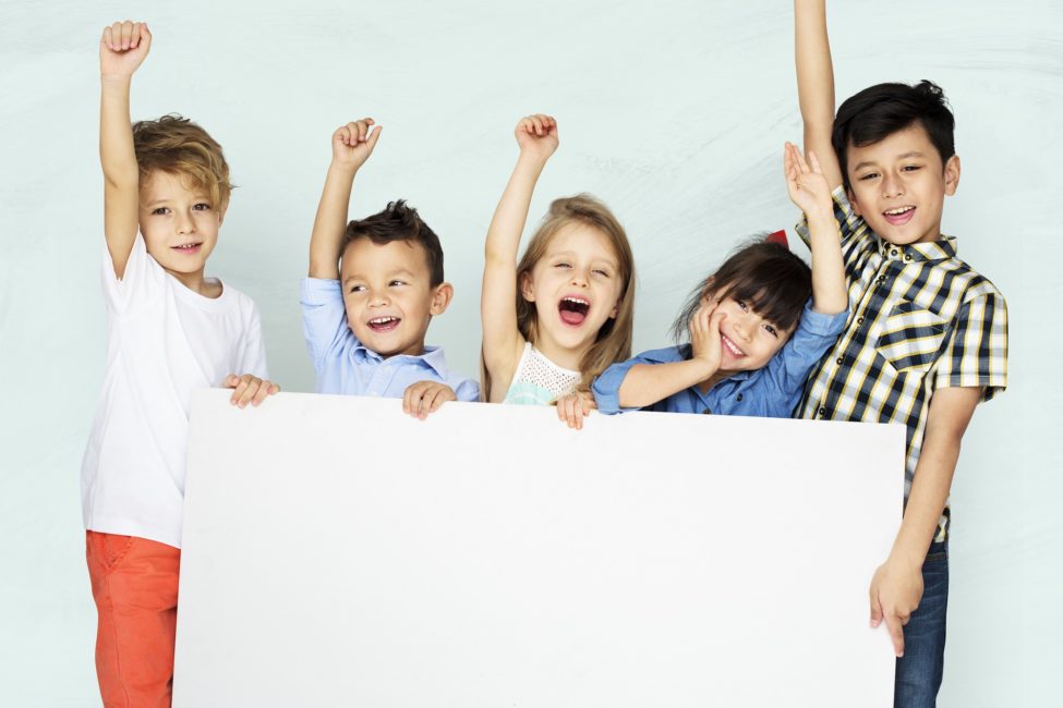 cinco crianças comemorando e segurando um quadro branco