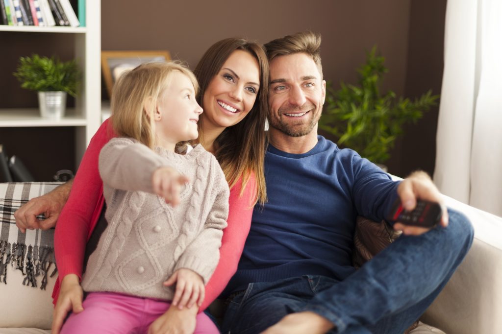 homem, mulher e uma menina loira todos sorrindo reunidos na sala