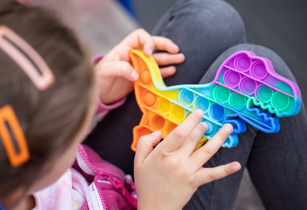 uma menina brincando com um fidget colorido em forma de dragão