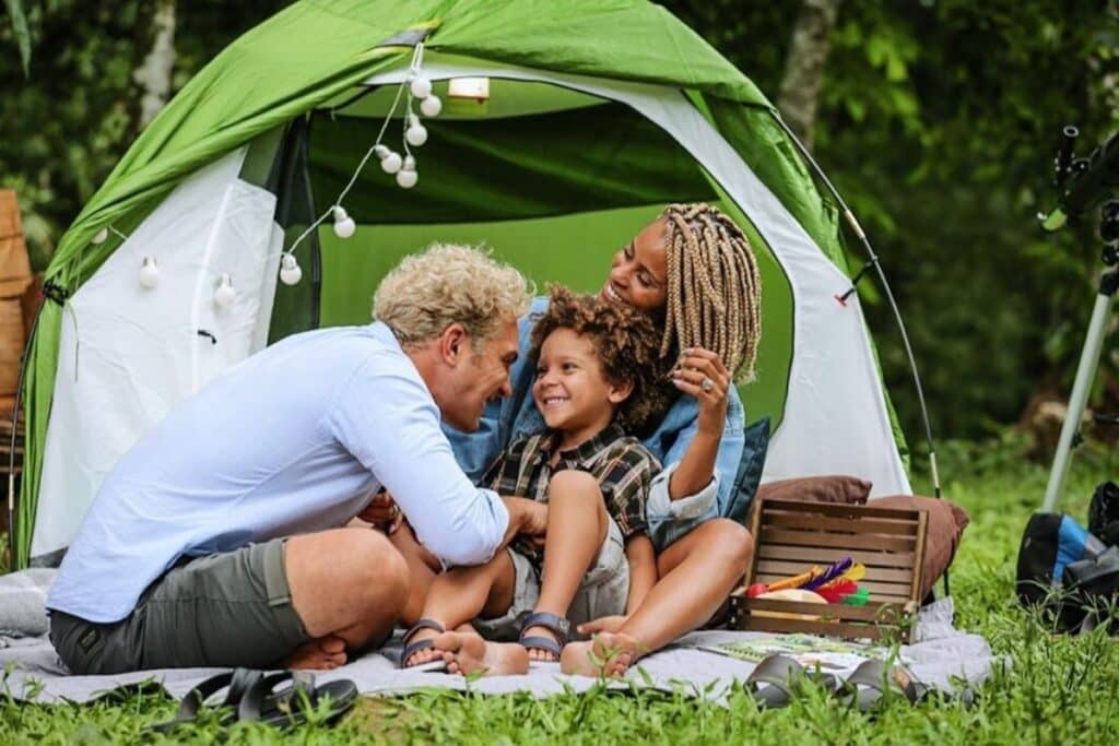 Filhos dos participantes do BBB23: A imagem mostra a atriz e cantora Aline e o ator Igor, com seu filho Antonio. Ambos estão em barraca em um local aberto com gramado. 