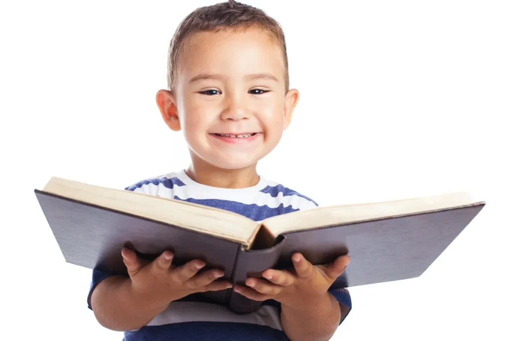 Menino pequeno segurando um livro aberto e sorrindo durante a leitura