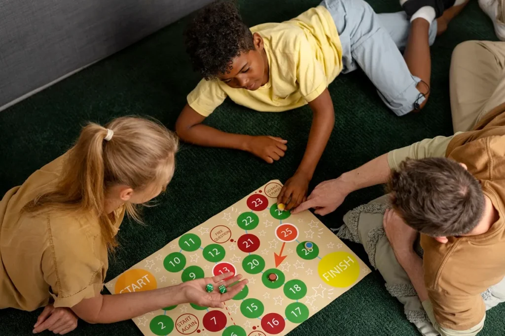 Crianças e um adulto jogando jogo de tabuleiro educativo no chão, promovendo aprendizado, raciocínio lógico e interação familiar.