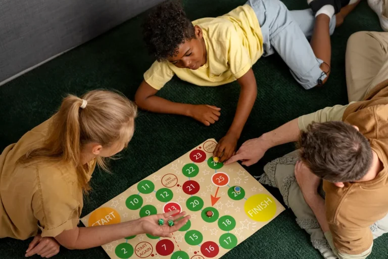 Crianças e um adulto jogando jogo de tabuleiro educativo no chão, promovendo aprendizado, raciocínio lógico e interação familiar.