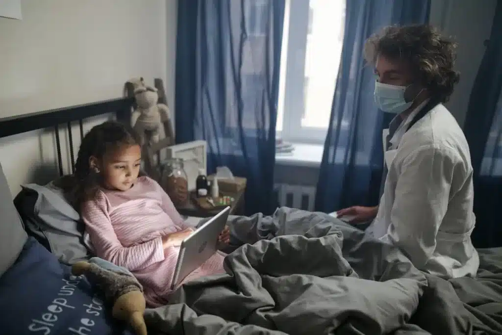 Criança doente deitada na cama sendo acompanhada por médico com máscara, representando cuidados em casos de meningite bacteriana.