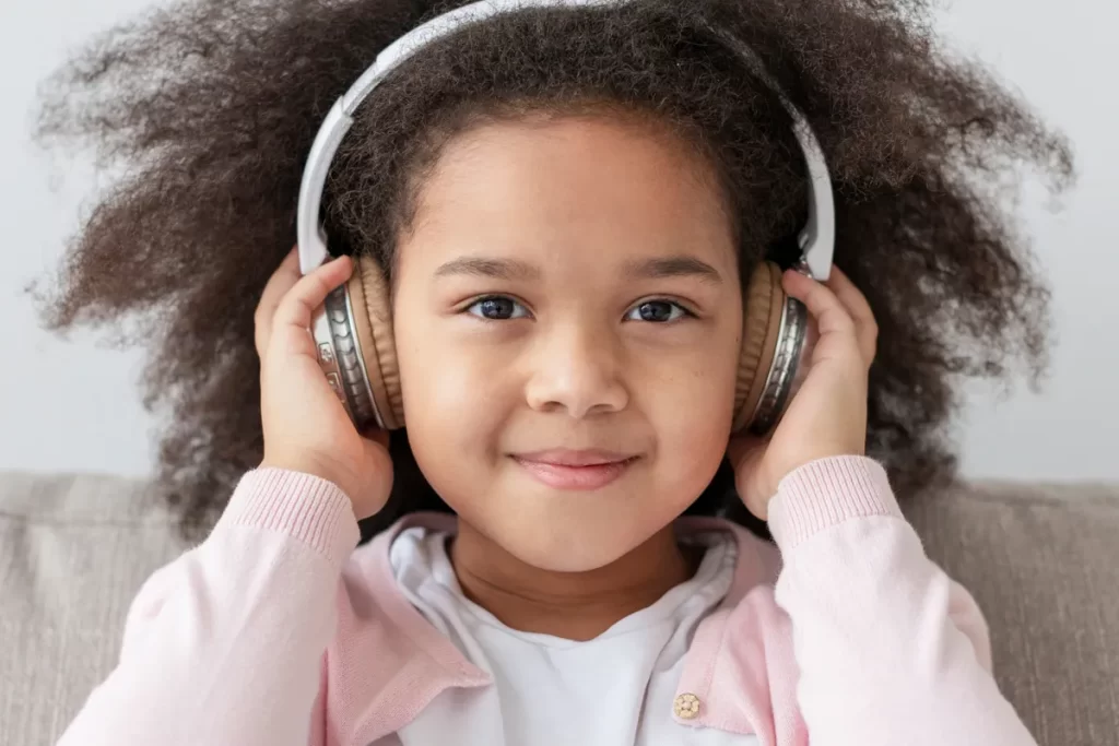 Menina sorrindo enquanto escuta músicas infantis com fones de ouvido grandes